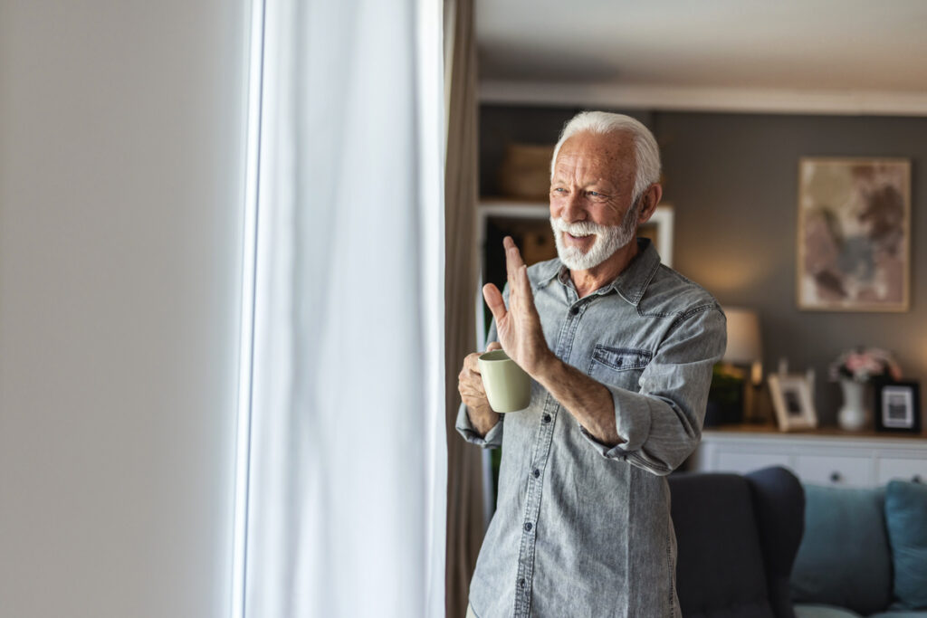 Älterer Mann winkt am Fenster